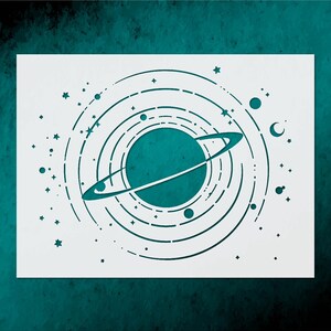 May include: A white stencil featuring a teal planet with rings, surrounded by concentric circles, stars, and celestial bodies. The design is cut out, creating a negative space effect. The stencil is on a teal background.