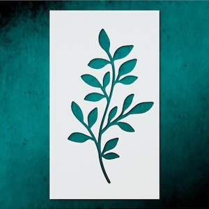 May include: A white rectangular stencil featuring a teal-colored botanical design of a leafy branch. The branch has multiple leaves and is centered on the stencil. The background is a textured teal color.
