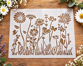 Puede incluir: Una plantilla rectangular de plástico blanco con un diseño detallado cortado con láser de un prado de flores silvestres. El patrón incluye varios tallos, hojas, hierbas y múltiples cabezas de flores de diferentes formas y tamaños.