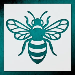 May include: A teal-colored bee stencil cut out of white material. The bee has detailed wings, antennae, and a striped abdomen. The stencil is set against a teal background, creating a contrast.