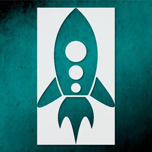 May include: A white stencil of a rocket ship against a teal background. The rocket has a pointed top, three circular windows, and angled fins. The background has a textured, mottled appearance.