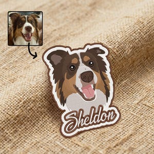 Op de afbeelding: Geborduurde patch met een honden gezicht met bruin, wit en bruin haar, en de naam "Sheldon" in een cursief lettertype. De patch heeft een witte rand en een bruine achterkant. Een kleine foto van de hond staat in de linkerbovenhoek.