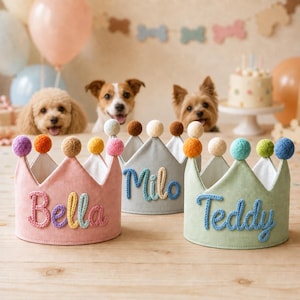May include: Three fabric crowns in pink, light gray, and light green, each featuring a white interior lining and a pom-pom on every point. The crowns are personalized with the names Bella, Milo, and Teddy in raised, knitted blue and yellow lettering.