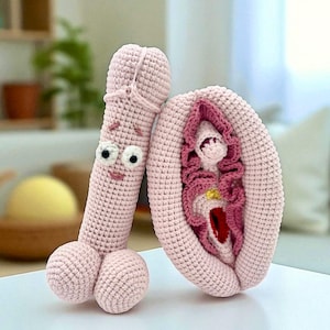 May include: A pair of handmade, light pink crochet sculptures. One is a stylized penis with a smiling face and googly eyes. The other is a stylized vulva with detailed interior features. The items are designed to be whimsical and decorative.