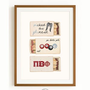 May include: Framed print featuring three matchbox designs. The top box reads "picked the finest" with angel wings. The middle box says "pi beta phi" with pool balls. The bottom box has "ΠΒΦ". The print is in a brown frame.