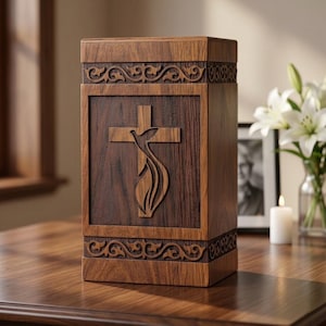 Könnte beinhalten: Holzurne mit geschnitztem Kreuz- und Taubendesign. Die rechteckige Urne hat verzierte Schnörkel an der Ober- und Unterseite. Das Kreuz und die Taube sind in eine dunklere Holzplatte auf der Vorderseite geschnitzt.