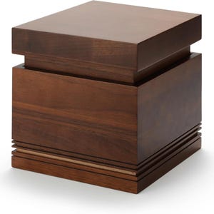 May include: A dark brown wooden box with a square shape. The box has a layered design, with a top section that overhangs the main body. The base features horizontal grooves and a thin, lighter-colored accent.