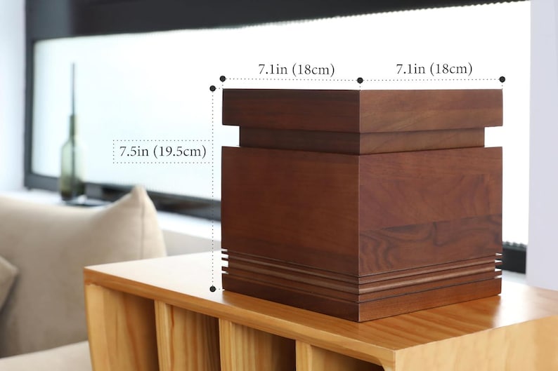 May include: A dark brown wooden box, 7.1 inches (18cm) wide and 7.5 inches (19.5cm) tall, with a layered design. The box is sitting on a light brown wooden surface. The box has a rectangular shape and is likely used for storage or display.