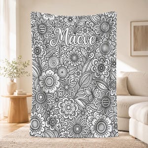 May include: A black and white throw blanket featuring a dense, intricate pattern of various stylized flowers, leaves, and circular motifs. The name Maeve is printed in a large, cursive script font across the upper center of the floral design.