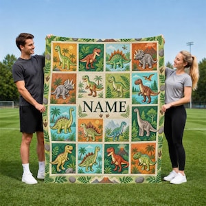May include: A rectangular quilt featuring a grid of twelve colourful illustrations of various dinosaurs in natural settings, with the word NAME printed in large black capital letters in the centre of the design, surrounded by a green leaf border.