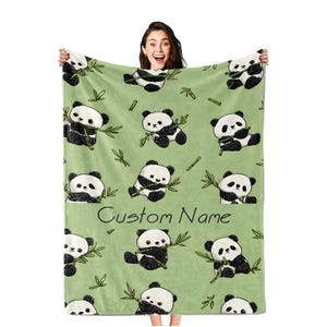 Peut inclure: Une couverture vert clair avec un motif répété d'ours pandas noirs et blancs tenant du bambou. La couverture porte l'inscription "Custom Name". Les pandas sont dans différentes poses, avec des feuilles de bambou éparpillées.