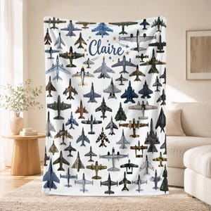 May include: A white fleece blanket featuring a repeating pattern of various military and commercial aircraft in shades of gray, blue, green, and brown. The name Claire is printed in a dark blue script font in the center, surrounded by small stars.