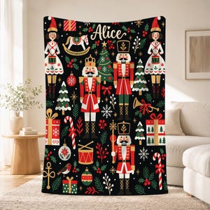 Puede incluir: Una manta polar negra con un patrón navideño repetitivo de cascanueces, soldados de juguete, árboles de pino decorados, cajas de regalo, bastones de caramelo, tambores y acebo. El nombre Alice está impreso en blanco en el centro superior.