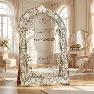 Pode incluir: Uma grande placa de casamento em forma de arco, com detalhes florais e o texto "Welcome to the Wedding of Alexander & Maria, June 14th 2026." A placa é emoldurada com um delicado design floral e está em uma sala clara.