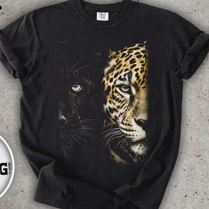 Può includere: T-shirt nero con una grafica raffigurante un volto di pantera e leopardo. La parola "BLACK" è stampata in alto. La maglietta ha maniche arrotolate e scollo tondo. La maglietta è su sfondo grigio.