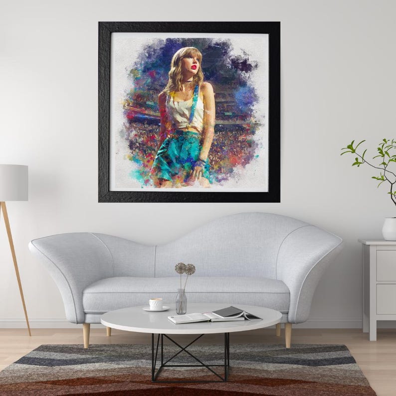 May include: Framed art print featuring a watercolor-style portrait of a woman in a white top and teal skirt with suspenders. The artwork is set against a colorful, abstract background and framed in black. The print is displayed above a gray sofa.