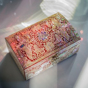 May include: A rectangular jewelry box featuring a deep red surface inlaid with iridescent mother-of-pearl designs. The lid displays intricate patterns of cranes, flowers, and butterflies, finished with a silver-toned metal butterfly latch.