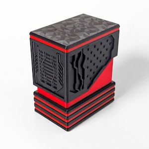 May include: A rectangular black and red storage box featuring a geometric patterned lid, vertical ribbed side panels, and a perforated section. The base consists of three stacked red and black horizontal layers, creating a structured, multi-tiered appearance.