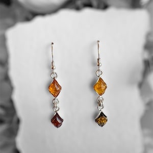 Può includere: Un paio di orecchini pendenti con ganci argentati e due pendenti a forma di diamante color ambra. Il pendente superiore è di un colore ambra più chiaro, mentre il pendente inferiore è di un colore ambra più scuro.