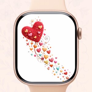 Könnte beinhalten: Eine Smartwatch mit einem Bildschirm, der ein rotes gehäkeltes Herz und eine Spur kleinerer Herzen in verschiedenen Farben zeigt. Die Uhr hat ein goldfarbenes Gehäuse und ein hellrosa Armband.