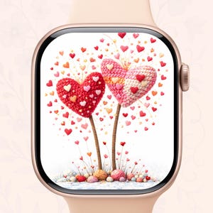 May include: A smartwatch with a screen displaying a heart-themed design. The design features two large, crocheted hearts in red and pink, with smaller hearts scattered around. The watch has a gold-colored case and a light pink band.