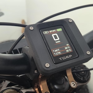 Può includere: Display digitale nero montato su un manubrio di bicicletta, che mostra 0 km/h. Il display mostra "SPORT" e letture della temperatura in gradi Celsius. Il marchio "TORP" è visibile in basso.