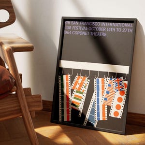 Op de afbeelding: Een ingelijste poster met een zwarte achtergrond en de tekst "3TH SAN FRANCISCO INTERNATIONAL FILM FESTIVAL OCTOBER 14TH TO 27TH 1964 CORONET THEATRE". De poster toont filmstrookontwerpen met verschillende kleuren en patronen.