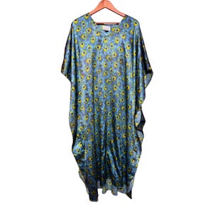 May include: A flowing, blue caftan with a vibrant peacock feather pattern. The design features yellow and blue accents, creating a striking visual effect. The caftan has a V-neck and wide sleeves, hanging from a wooden hanger.
