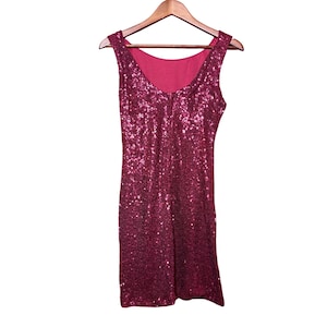 Könnte beinhalten: Ein ärmelloses, knielanges Kleid, das mit schimmernden, dunkelrosa Pailletten bedeckt ist. Das Kleid hängt an einem Holzbügel vor einem weißen Hintergrund. Das Kleid hat einen Rundhalsausschnitt und ein einfarbiges rosa Futter.