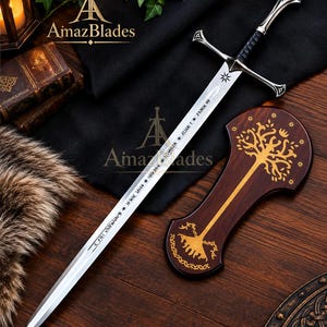 May include: A silver-toned metal sword with a black leather-wrapped grip, a cross-guard, and a pommel. The blade features engraved runic text and a star symbol. Beside the sword lies a dark wooden plaque decorated with a gold-coloured tree design.