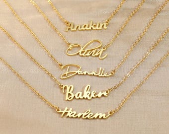 May include: Five gold-colored name necklaces with delicate chains. Each necklace features a different name: Anakin, Starr, Danielle, Baker, and Harlem, in a cursive font. The necklaces are displayed on a neutral-toned background.