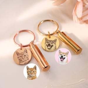 Puede incluir: Llaveros con retratos de mascotas grabados. Los llaveros presentan un colgante circular con la imagen de una mascota, un recipiente cilíndrico y un llavero. Los llaveros son en tonos dorados y oro rosa, con imágenes de gatos y perros.