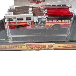 May include: A die-cast model fire engine, predominantly red and white, with the number 47 displayed. The model includes a ladder and the word "FIRE". The packaging features the text "CODE 3 FIRE ENGINE". The model is a collectible.