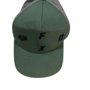 Könnte beinhalten: Grüne und graue Baseballkappe mit den Buchstaben "F" und "X" in Marineblau. Die Kappe hat auch ein marineblaues Fuchlogo. Die Kappe hat einen gebogenen Schirm und eine Mesh-Rückseite.