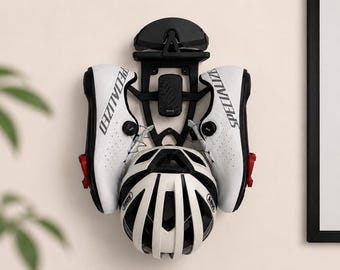 May include: A black wall-mounted storage rack holding a pair of white Specialized cycling shoes with red cleats, a white Abus bicycle helmet, a pair of black cycling sunglasses, and a small black electronic device centered on the frame.