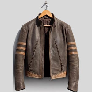 Può includere: Una giacca in pelle marrone scuro con colletto alla coreana, chiusura frontale con zip e due tasche verticali con zip. Le maniche sono caratterizzate da tre strisce orizzontali in pelle beige e l'orlo presenta un inserto in pelle beige.