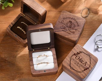 May include: Wooden ring boxes, some open to display gold rings with intricate designs and a diamond. The boxes are engraved with names and dates, perfect for weddings or anniversaries. The boxes are made of dark wood.