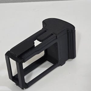 Peut inclure: Un cadre ou bo&icirc;tier de protection noir, rectangulaire et imprim&eacute; en 3D pour un petit appareil &eacute;lectronique. L'objet pr&eacute;sente une conception en cage &agrave; c&ocirc;t&eacute;s ouverts avec une section de poign&eacute;e solide et profil&eacute;e &agrave; une extr&eacute;mit&eacute;.
