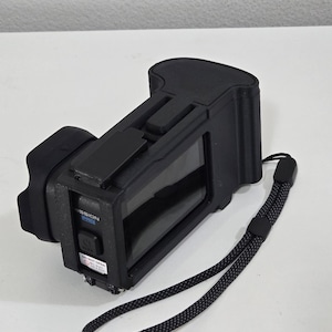 Peut inclure: Un appareil &eacute;lectronique noir avec un &eacute;cran rectangulaire, une poign&eacute;e textur&eacute;e et une dragonne. Le c&ocirc;t&eacute; pr&eacute;sente un bouton d'alimentation, une &eacute;tiquette bleue MISSION PRO et un autocollant d'avertissement blanc DO NOT OPEN en noir.