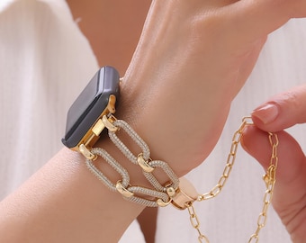 May include: A gold-toned watch band with a chain-link design. The band features a series of interconnected oval links, some encrusted with small, sparkling stones. The watch face is dark gray. A small chain dangles from the band.
