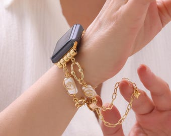 Puede incluir: Correa de reloj dorada con diseño de cadena, con detalles de perlas blancas. La correa está sujeta a un reloj inteligente gris oscuro. La cadena tiene un pequeño dije al final.