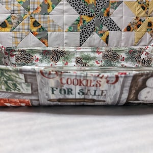 May include: Rectangular glass baking dish with a fabric cover featuring a Christmas-themed design. The fabric displays pine cones, berries, and a snowman with the text "COOKIES FOR SALE".