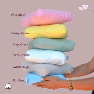 Può includere: Una pila di sei cuscini quadrati in vari colori pastello: rosa blush, giallo sole, verde salvia, crema avorio, beige caldo e azzurro cielo. Ogni cuscino ha un aspetto morbido e soffice. I cuscini sono etichettati con i rispettivi nomi di colore.