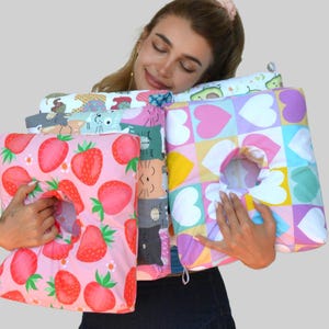 May include: A collection of colorful pillows with various patterns, including strawberries, cats, avocados, and hearts. Each pillow has a circular opening. The pillows are in shades of pink, green, blue, yellow, and purple.