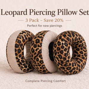 Puede incluir: Tres almohadas en forma de rosquilla con estampado de leopardo. Las almohadas tienen un panel lateral beige y están diseñadas para la comodidad de la perforación. El texto de la imagen dice "Leopard Piercing Pillow Set" y "Complete Piercing Comfort."