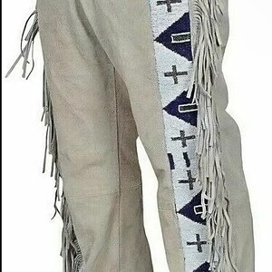 May include: Light gray suede pants with decorative fringe along the sides. The pants feature a beaded design with crosses and triangles in white, navy blue, and black. A traditional Western wear item.