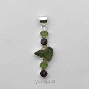 May include: A silver pendant featuring a series of green and dark brown gemstones. The pendant has a rectangular bail and a large, irregularly shaped green stone in the center. The text "Silver Studio 25" is at the bottom.