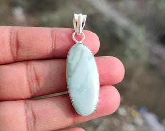 May include: A light blue oval pendant with a silver bail. The pendant has a marbled appearance with shades of white and light blue. The pendant is held in a hand. The text "925 Silver Legacy" is at the bottom.