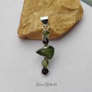 May include: A silver pendant featuring a series of green and brown gemstones. The pendant has a rectangular bail and a vertical design with a large, irregularly shaped green stone at the center. The text "Silver Studio 25" is at the bottom.