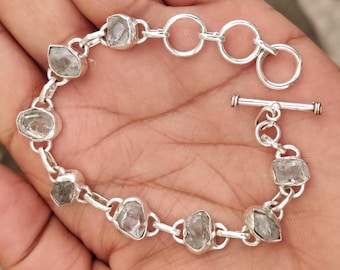 May include: A silver bracelet featuring irregularly shaped, light gray gemstones. The bracelet is composed of individual links connecting the stones, with a toggle clasp. The gemstones are set in silver bezels.